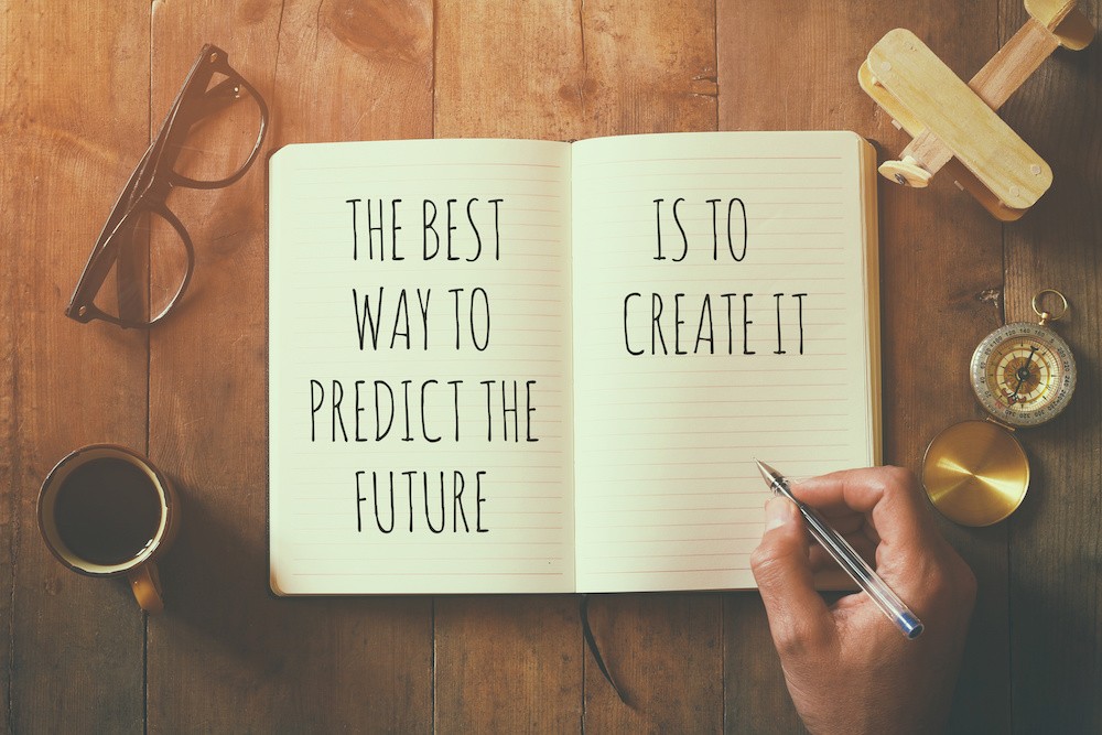 open notebook over wooden table with motivational saying the best way to predict the future is to create it