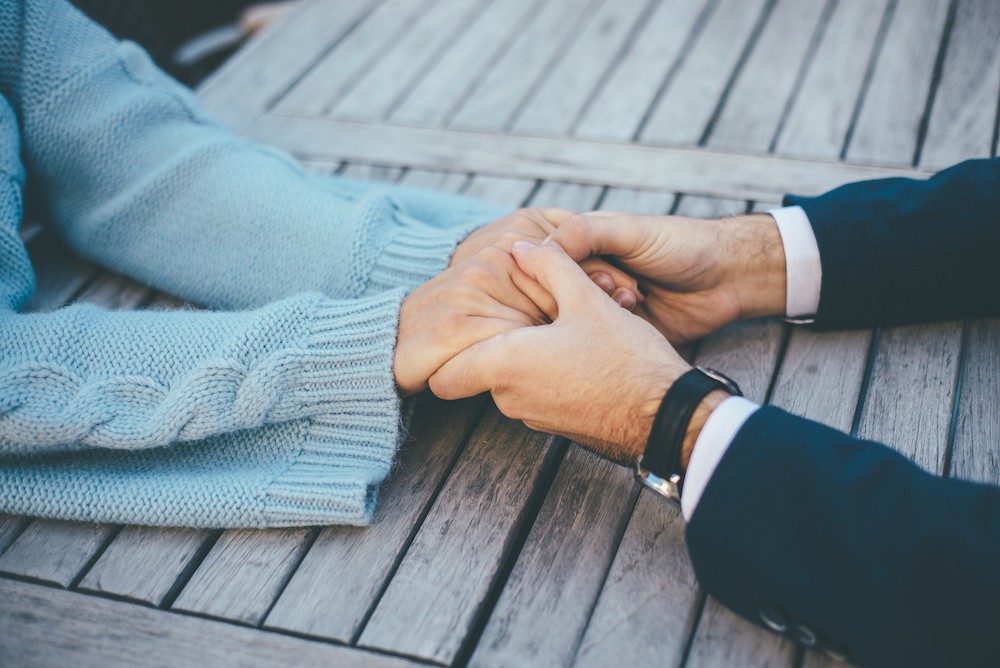 Two persons in love hold their hands on the wooden table, close up image