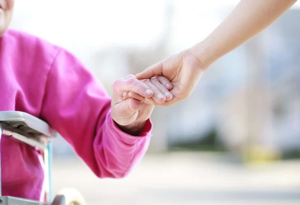 Senior Lady in Wheelchair Holding Hands with Caretaker