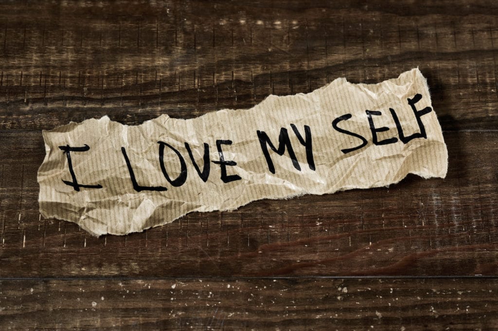 the text I love myself written in a piece of paper, placed on a rustic wooden surface